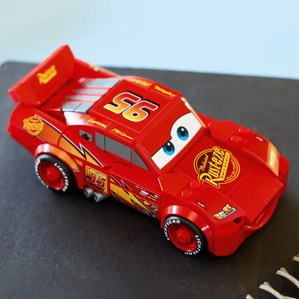 Completed LEGO Lightning McQueen model displayed on a dark surface, highlighting the red bodywork, Rust-eze hood logo, number 95 markings, rear spoiler, and detailed wheels from an angled view