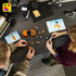 LEGO Speed Champions Toyota Supra MK4 build scene shows two people assembling the orange brick car with loose pieces and tablets displaying digital instructions on a dark workbench.