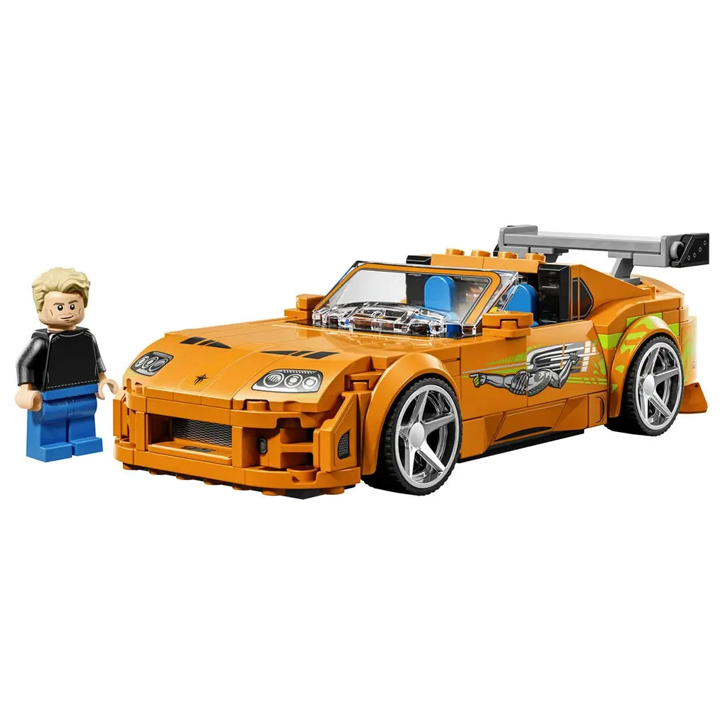 LEGO Speed Champions Toyota Supra MK4 in orange plastic features silver wheels, green side graphics, clear engine details and a gray rear wing beside a driver minifigure.