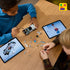 Two children building the LEGO Back to the Future Time Machine at a wooden table, with gray car parts, loose bricks, minifigures, and tablets showing step-by-step digital building instructions