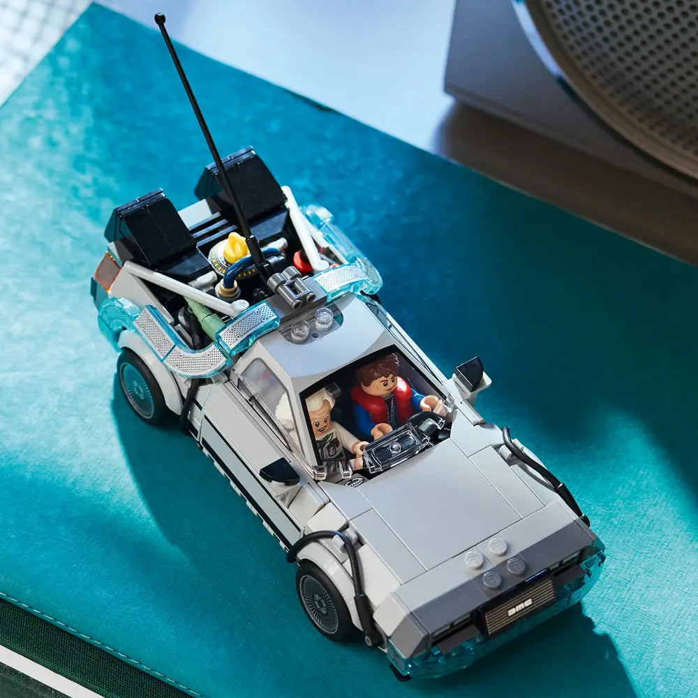 Completed LEGO Back to the Future Time Machine displayed on a teal surface, featuring the gray DeLorean body, roof-mounted components, rear reactor assembly, and seated Marty McFly and Doc Brown minifigures