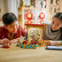 Two children smiling as they assemble the LEGO Galloping Horses Canvas, with multicolored plastic bricks, horse figures, and festive red decorations displayed in a cozy home environment