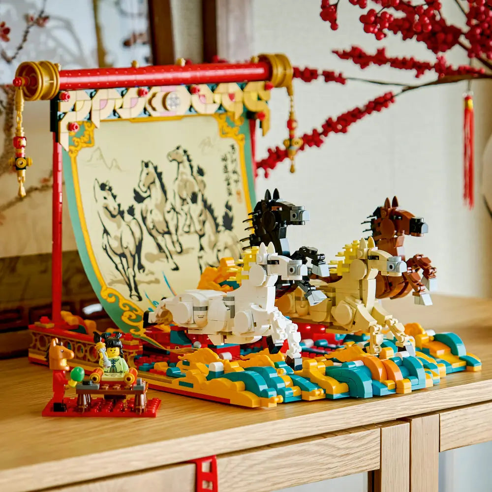 Completed LEGO Galloping Horses Canvas displayed on a wooden table, featuring red and gold scroll details, four running horses, teal wave base, and Spring Festival decor in the background