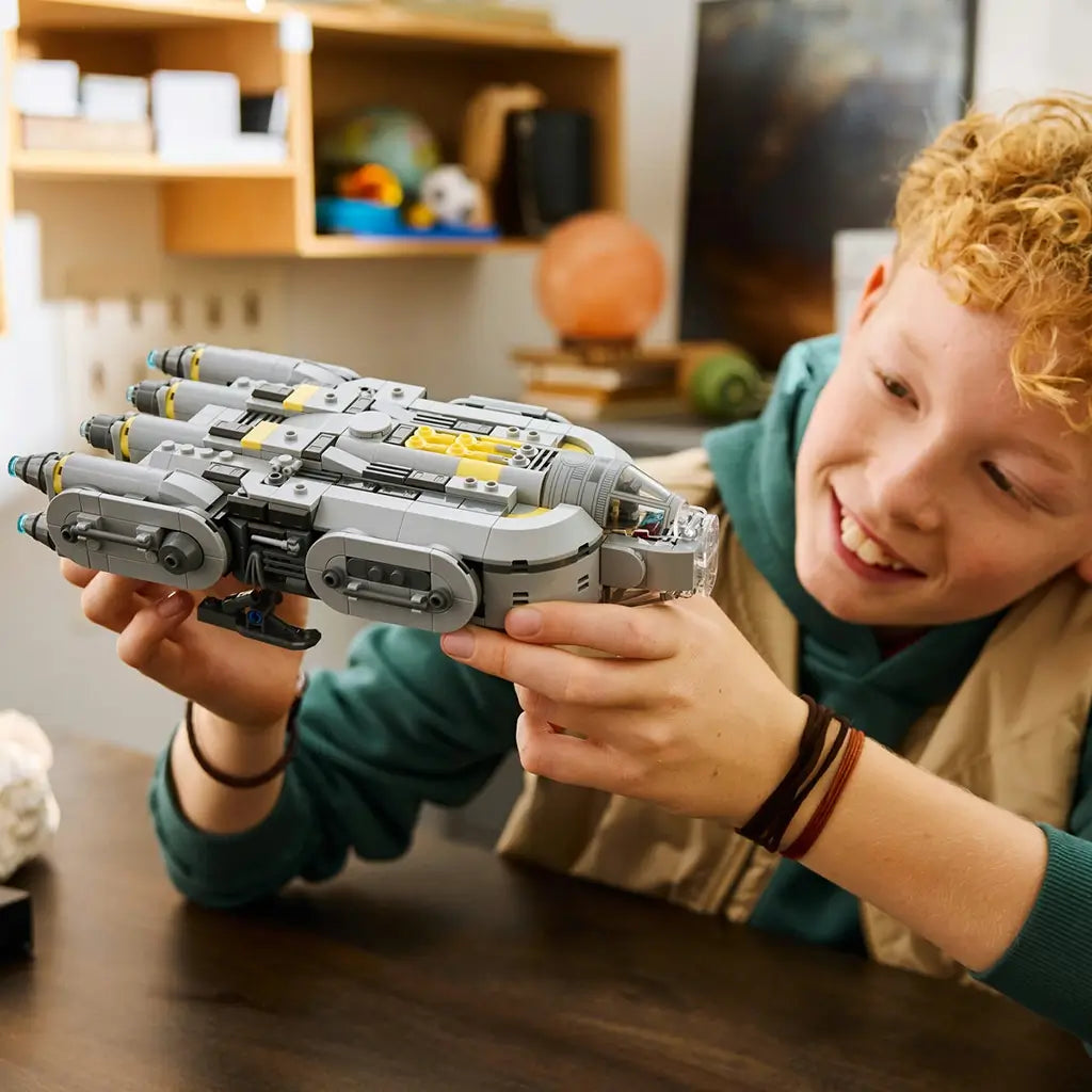 LEGO Star Wars Anzellan Starship model features a gray plastic spacecraft with rounded engines and yellow accent details, held by a child in a home setting while imagining flight adventures.