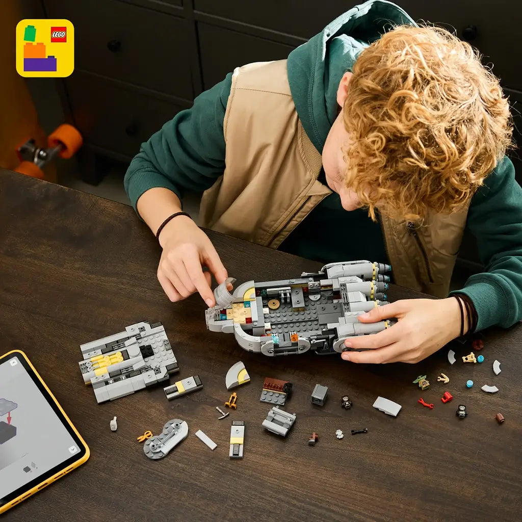 LEGO Star Wars Anzellan Starship building set shows gray plastic spacecraft sections with yellow accents and detailed interior parts, being assembled on a dark wooden table beside a mobile device.