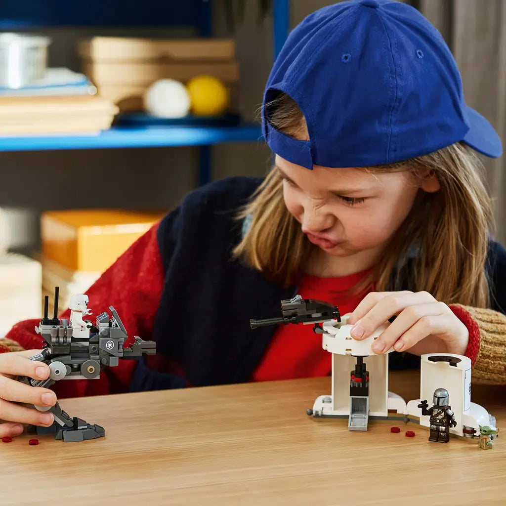 LEGO Star Wars AT-RT Attack play scene shows a child using a gray plastic walker and white turret build with minifigures, recreating action adventures on a tabletop indoors.