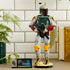LEGO Star Wars Boba Fett display figure in green, gray, red and yellow plastic bricks, holding a black blaster beside a minifigure and plaque in a bright indoor setting.