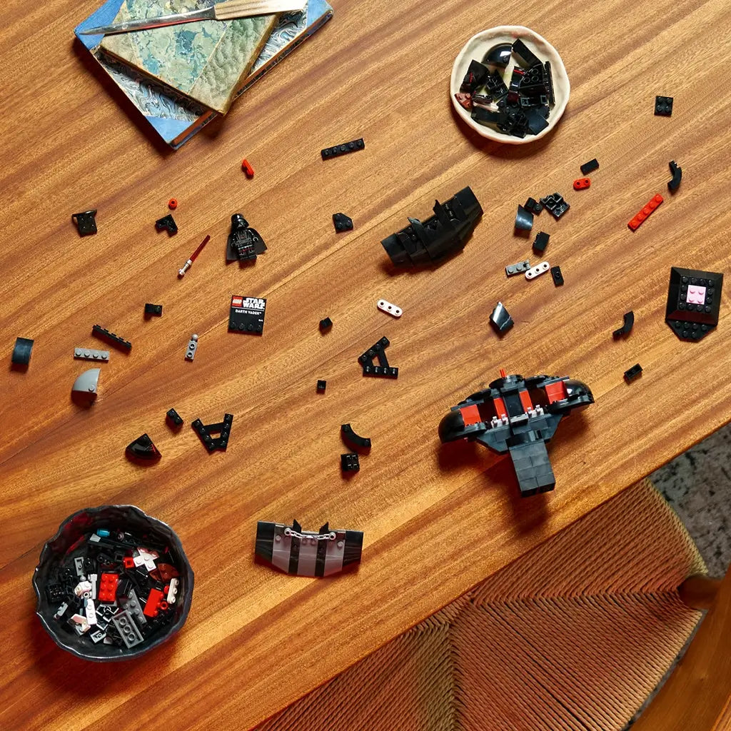 LEGO Star Wars Darth Vader building set shows black plastic model sections, curved armor pieces and minifigure components arranged across a wooden table during assembly.