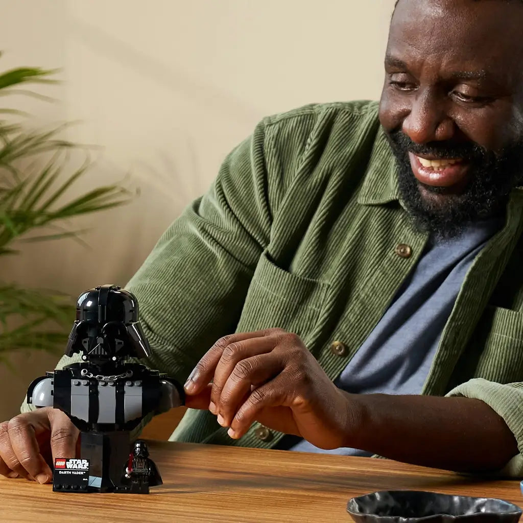 LEGO Star Wars Darth Vader collectible bust features glossy black plastic armor shapes and a helmet display, shown being adjusted by an adult on a tabletop in a home setting.