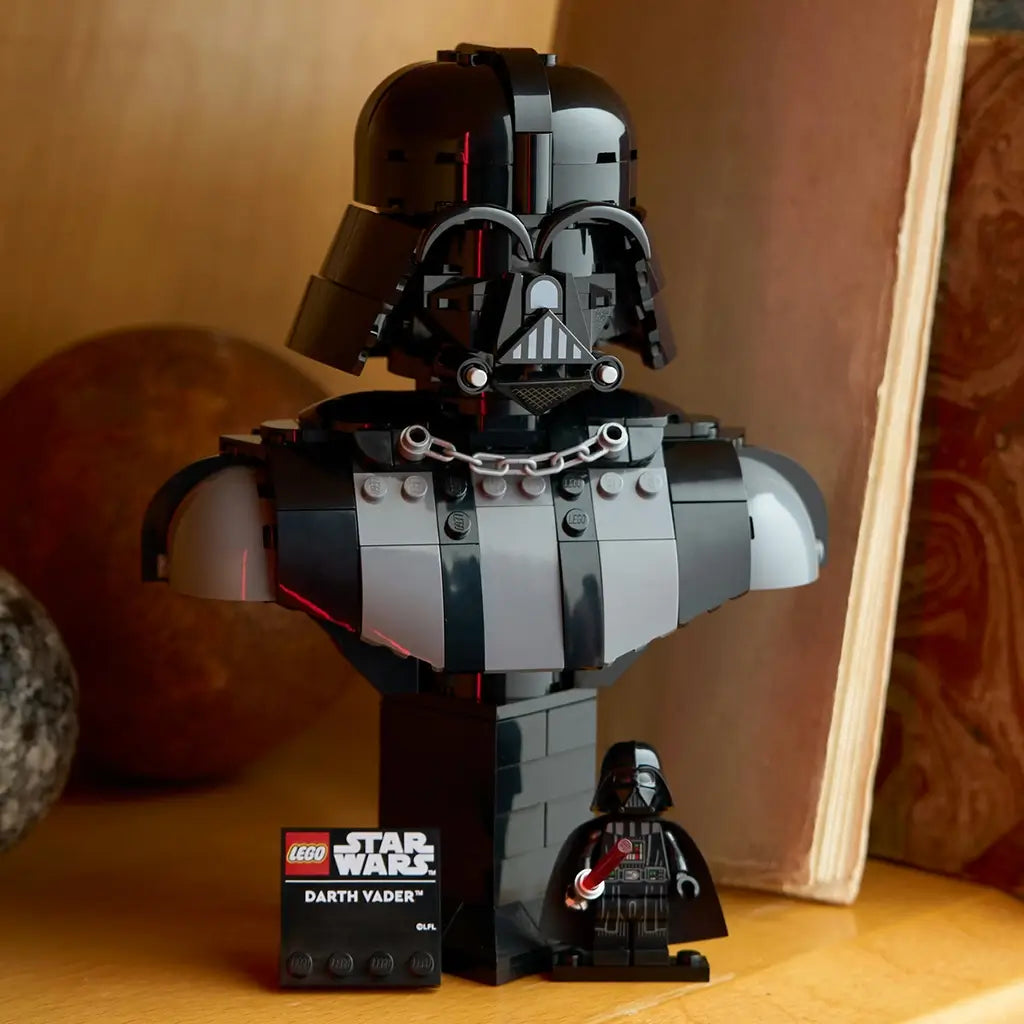 LEGO Star Wars Darth Vader display features glossy black plastic armor panels, a sculpted helmet bust, character plaque and minifigure, presented on a shelf beside books.