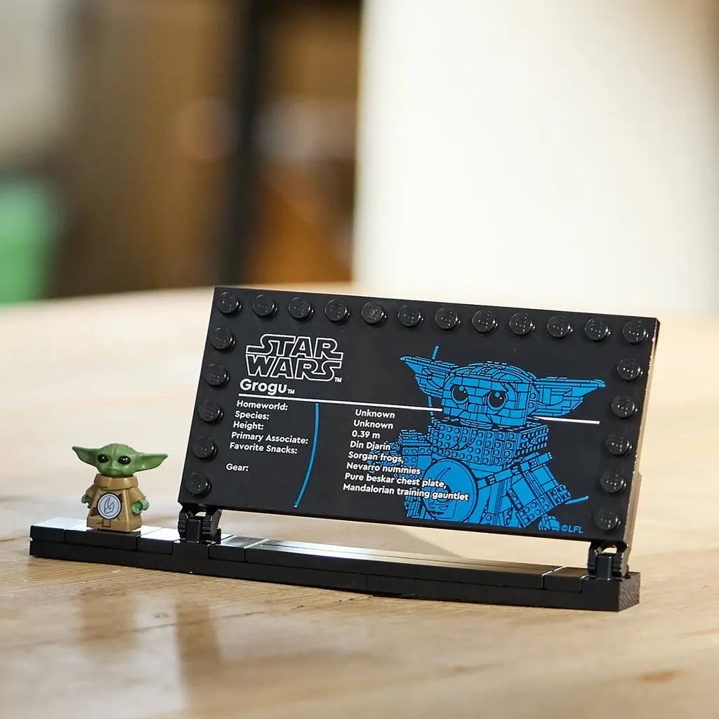 LEGO Star Wars Grogu display plaque features a black plastic information panel with blue character artwork, a small green Grogu minifigure, and a stand on a tabletop background.