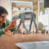 LEGO Star Wars Imperial Remnant AT-AT in gray plastic bricks stands on a wooden table as a builder adjusts the walker beside seven minifigures and the INT-4 vehicle.