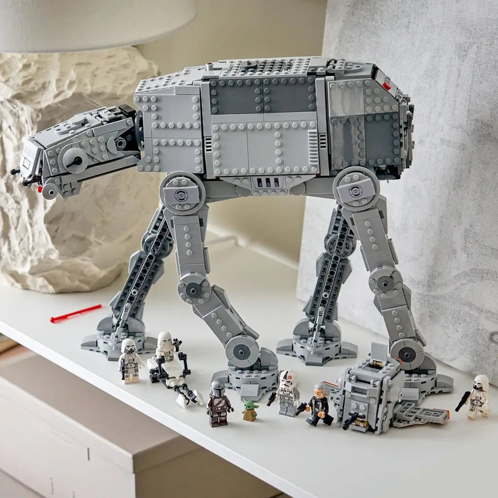 LEGO Star Wars Imperial Remnant AT-AT in light and dark gray plastic bricks is displayed on a white shelf with INT-4 vehicle and seven minifigures arranged below.