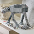 LEGO Star Wars Imperial Remnant AT-AT in light and dark gray plastic bricks is displayed on a white shelf with INT-4 vehicle and seven minifigures arranged below.