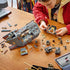 LEGO Star Wars Offworld Sandcrawler build in gray, tan and brown plastic is partly assembled across a wooden table as a young builder adds pieces beside minifigures and a tablet.