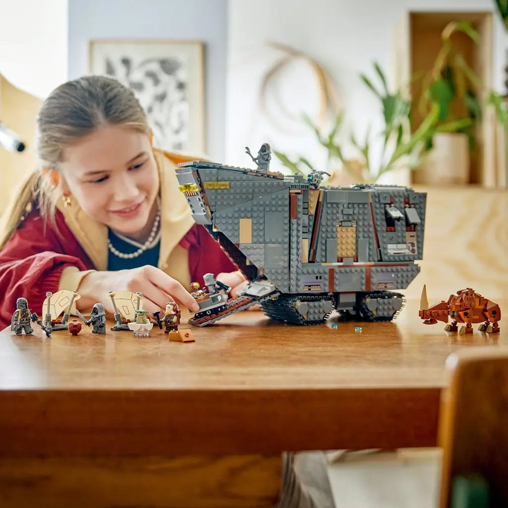 LEGO Star Wars Offworld Sandcrawler in gray plastic sits on a wooden table with minifigures and a brown Mudhorn as a young builder plays with its opening front ramp indoors.