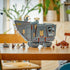 LEGO Star Wars Offworld Sandcrawler in gray plastic stands on black tracks with minifigures, Grogu, a cart and brown Mudhorn displayed across a wooden table in a bright room.