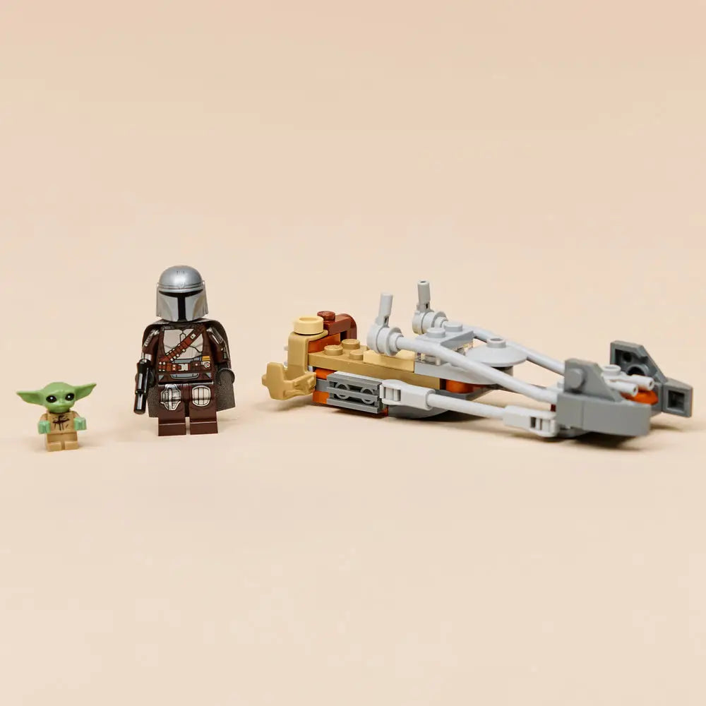 LEGO Star Wars Mandalorian speeder bike model in gray and tan plastic fully assembled, displayed with The Mandalorian and Grogu minifigures standing beside it on a smooth neutral tabletop.