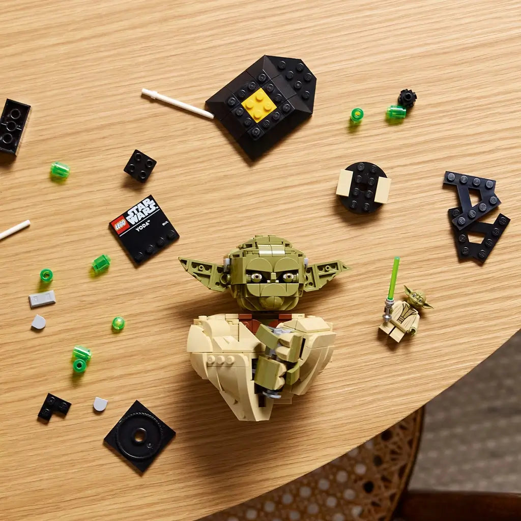 LEGO Star Wars Yoda building set shows olive green and tan plastic pieces, curved character sections and display components arranged for assembly across a wooden tabletop with a Yoda minifigure.