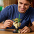 LEGO Star Wars Yoda collectible bust features olive green and tan plastic construction, a detailed Jedi character form with green lightsaber, displayed while being adjusted by a builder at a table.
