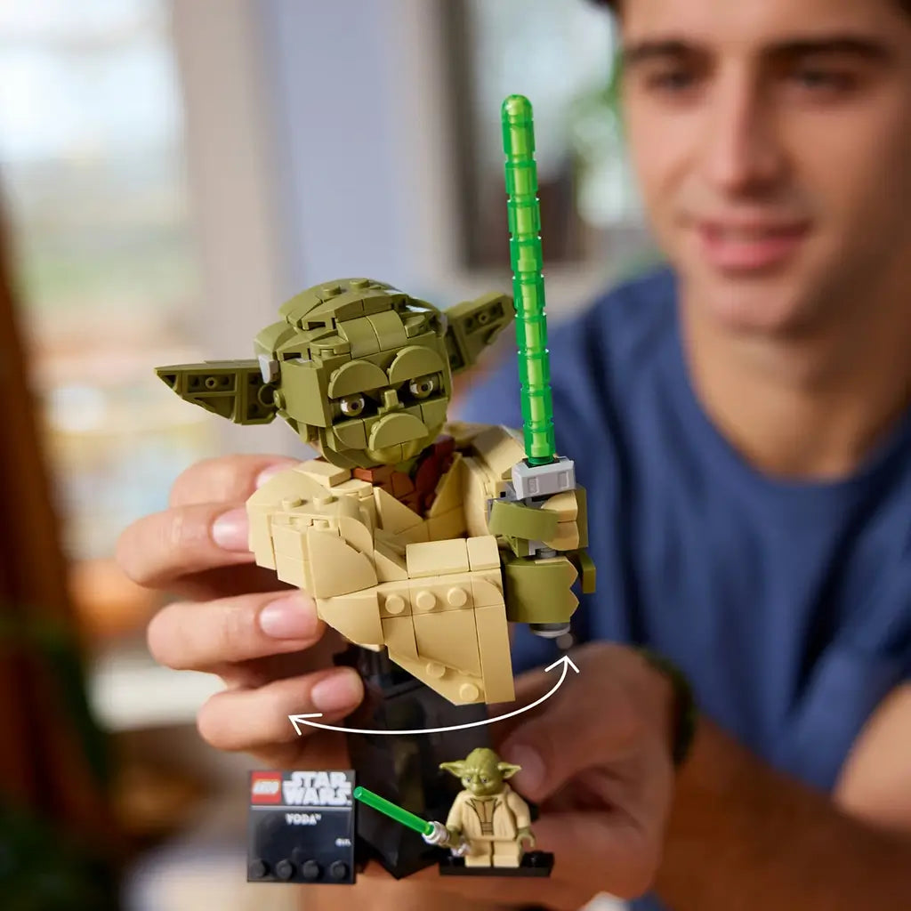 LEGO Star Wars Yoda bust features olive green and tan plastic textures, a rounded Jedi head and robe shape, movable display model with green lightsaber, shown in hand within a home setting.