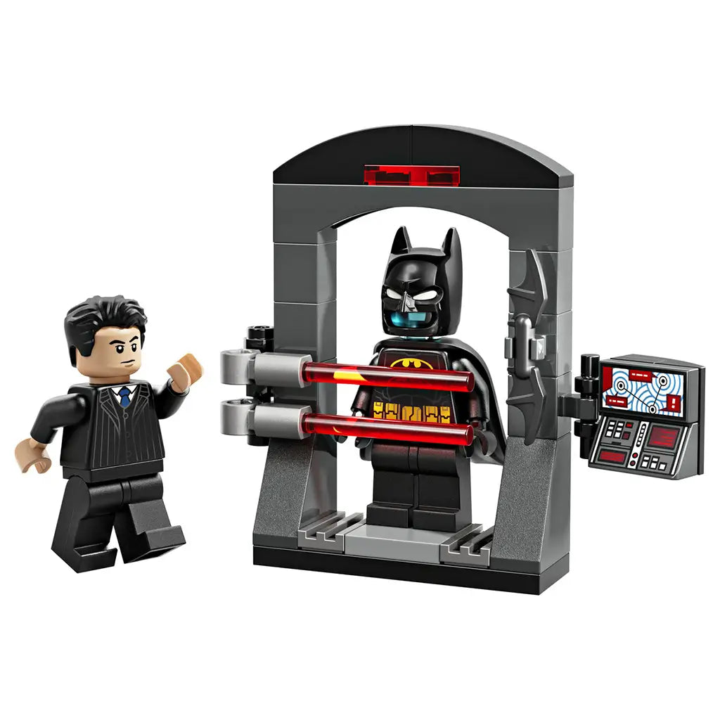 LEGO Batman Bruce Wayne and the Batsuit toy display showing black, gray, and red plastic bricks, Bruce Wayne minifigure, Batman minifigure inside a Batsuit chamber, control panel accessory, and dramatic play features on white.