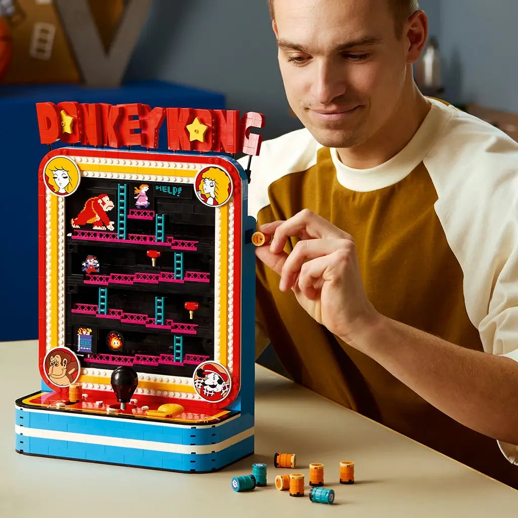 LEGO Donkey Kong Arcade in red, blue and black plastic bricks, played by an adult at a table while holding an orange barrel piece beside the retro game cabinet.