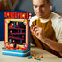 LEGO Donkey Kong Arcade in red, blue and black plastic bricks, played by an adult at a table while holding an orange barrel piece beside the retro game cabinet.
