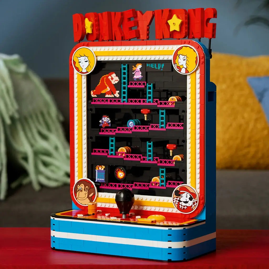 LEGO Donkey Kong Arcade in red, blue and black plastic bricks, displayed as a retro game cabinet with pixel characters, ladders and controls on a red table in a living room.