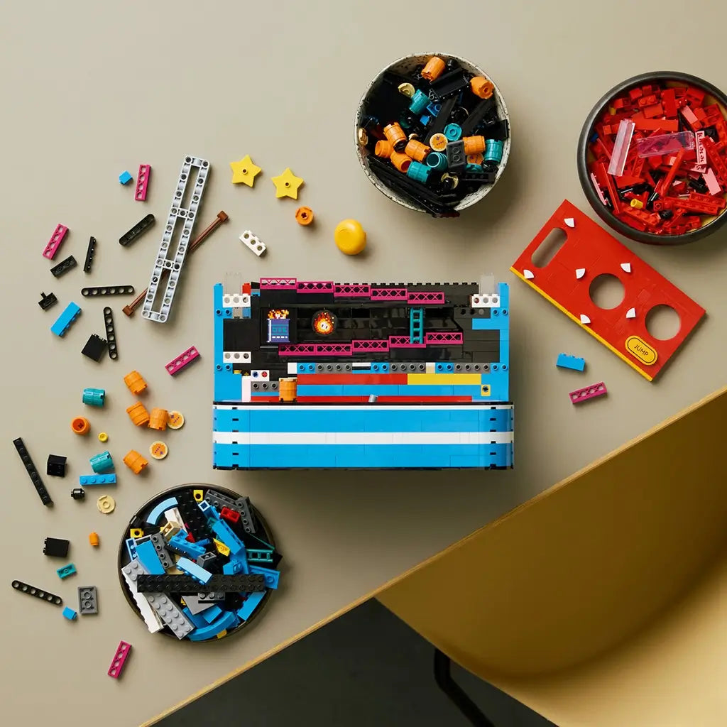 LEGO Donkey Kong Arcade build in blue, black and red plastic bricks, partially assembled from above among colorful beams, barrels, stars and trays of pieces on a tabletop.