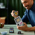 Smiling person assembling the LEGO Nintendo Game Boy model, inserting a brick-built The Legend of Zelda cartridge into the console replica during a hands-on build session.