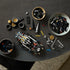 LEGO Technic Ford GT40 Mk II build activity shows black Technic beams, axles, gears, and gold wheel parts organized on a dark tabletop around a partially assembled chassis during focused construction.