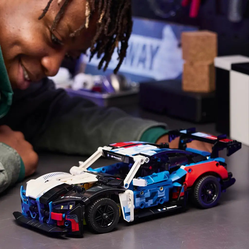 LEGO Technic BMW M4 GT3 EVO toy shows a multicolor plastic race car with blue, white, black, and red panels, explored by a child during play, demonstrating interactive building experience in a modern indoor setting.