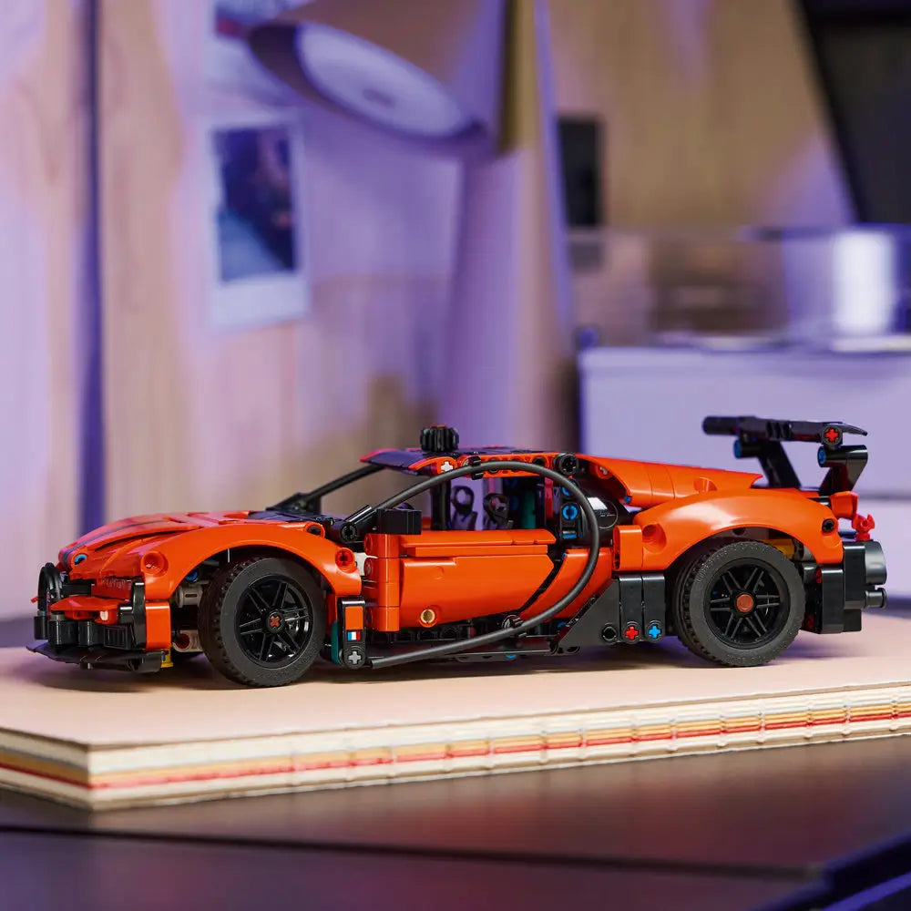 LEGO Technic Bugatti Chiron Pur Sport model displayed fully built with orange bodywork, black accents, rear wing, low stance, and realistic proportions positioned on stacked books in a creative workspace.