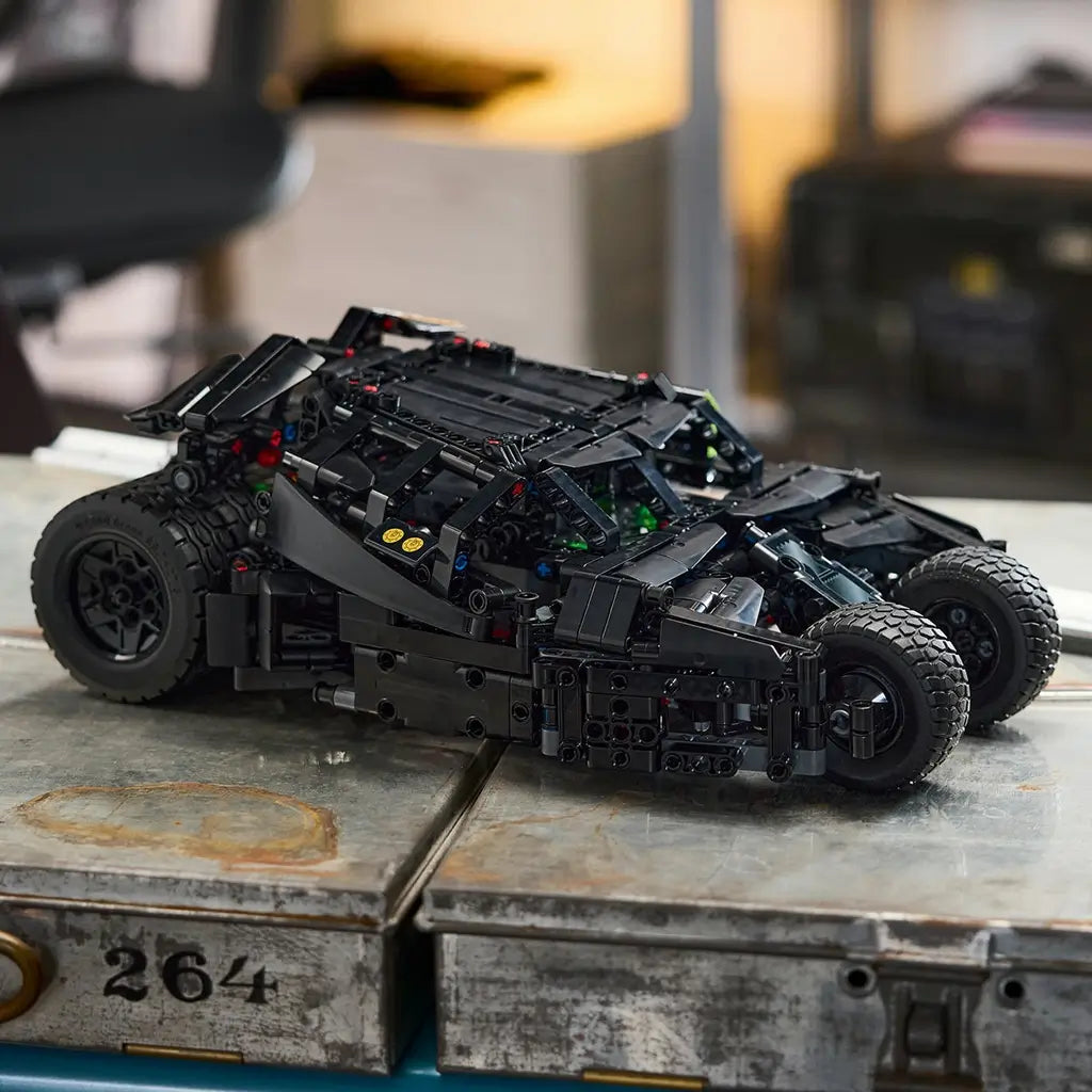 LEGO Technic Batmobile Tumbler model in black plastic features a low armored body and rugged tires, displayed on an industrial metal workbench in a workshop setting.