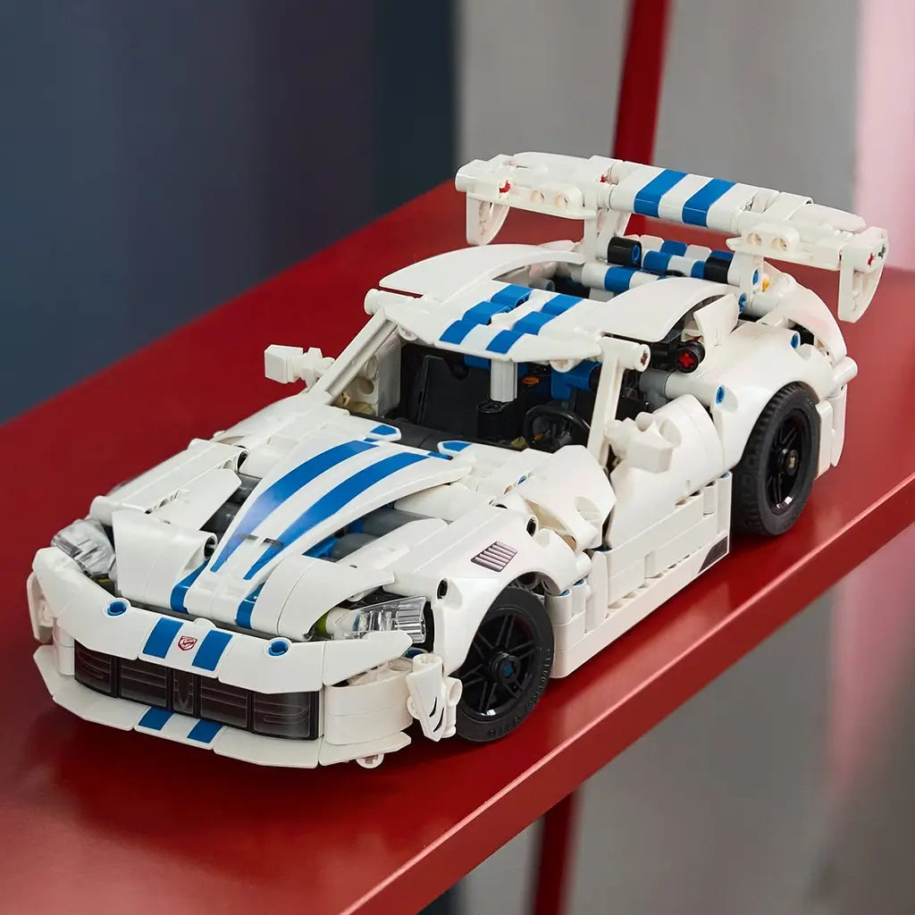 LEGO Technic Dodge Viper GTS-R model in white plastic with blue racing stripes, black wheels and a large rear wing is displayed on a red shelf in a colorful room.