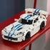 LEGO Technic Dodge Viper GTS-R model in white plastic with blue racing stripes, black wheels and a large rear wing is displayed on a red shelf in a colorful room.