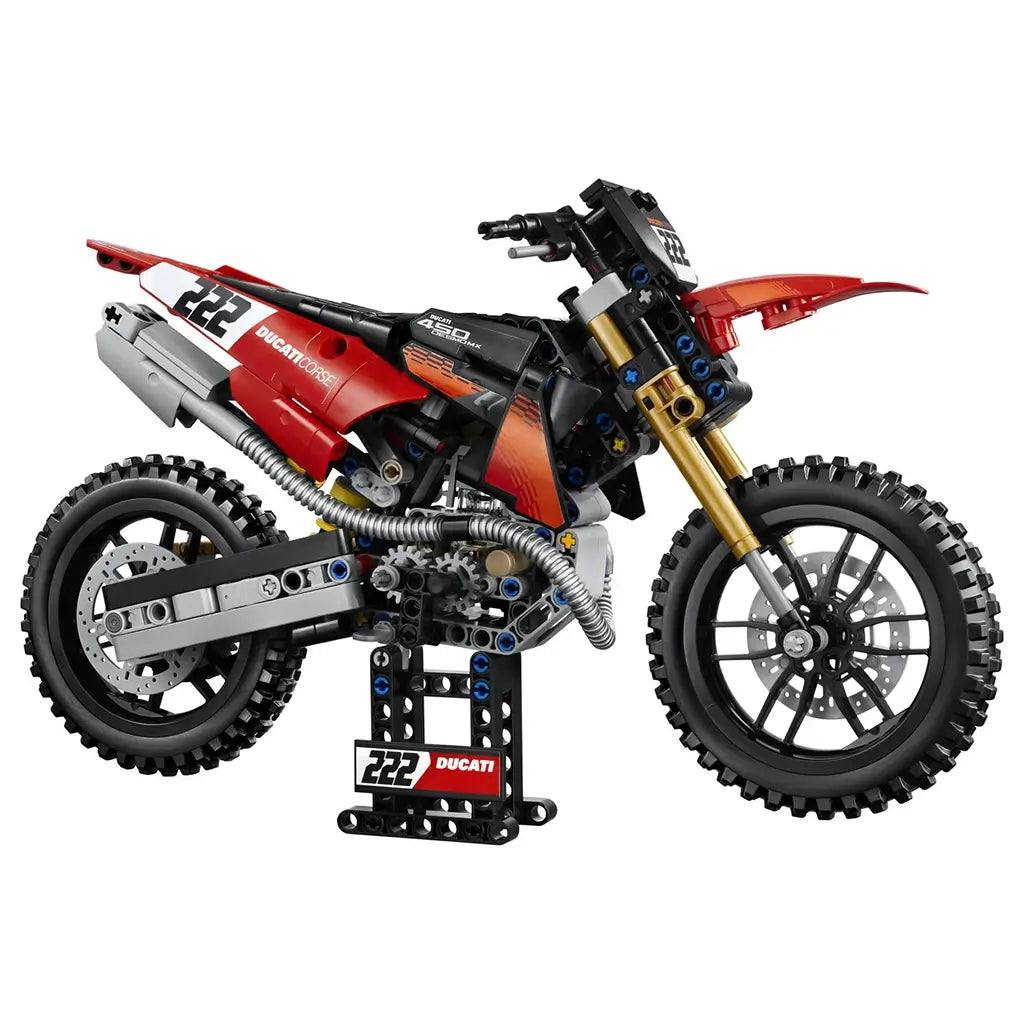 LEGO Technic Ducati Desmo450 MX Factory model in red, black, gold, and silver plastic features knobby tires, detailed engine parts, and a display stand on white.