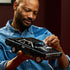 LEGO Technic Dodge Charger R/T in black plastic bricks with silver wheels and supercharger, held by an adult builder in a blue denim shirt against a dark red wall.