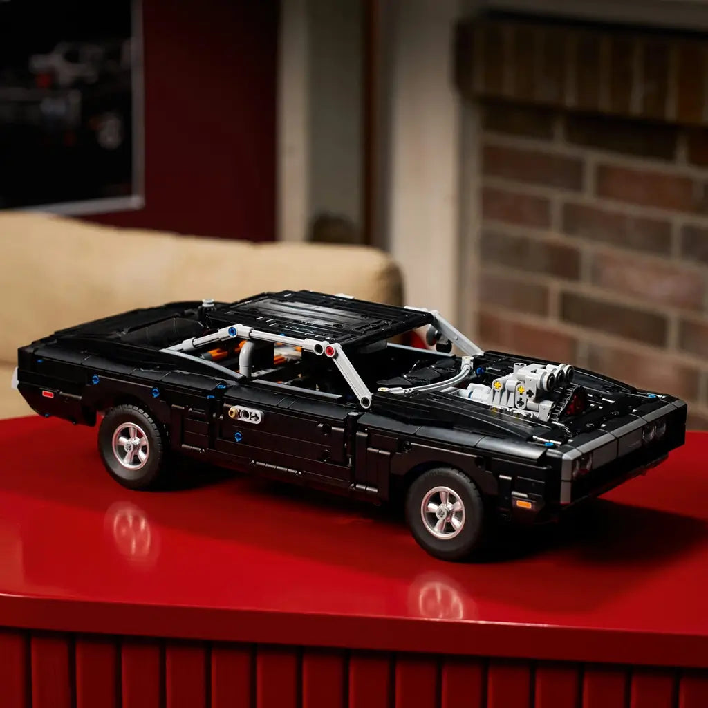 LEGO Technic Dodge Charger R/T in black plastic bricks with silver wheels and exposed engine, displayed on a glossy red table in a warm living room setting.