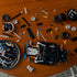 LEGO Technic Dodge Charger build in black plastic pieces, partially assembled from above amid tires, silver wheels, beams and connectors scattered across a wooden table.