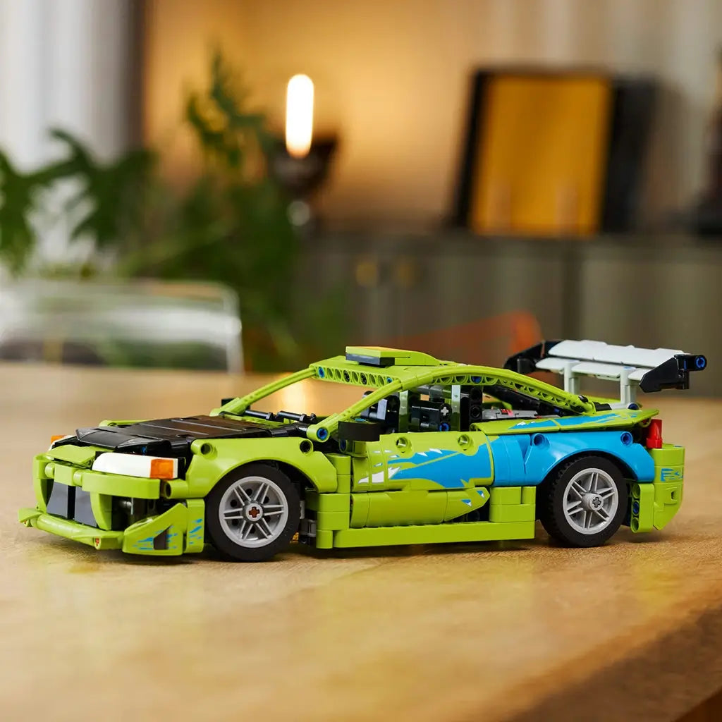 LEGO Technic Mitsubishi Eclipse in lime green and blue plastic bricks with silver wheels and rear wing, displayed on a wooden table in a softly lit home interior.