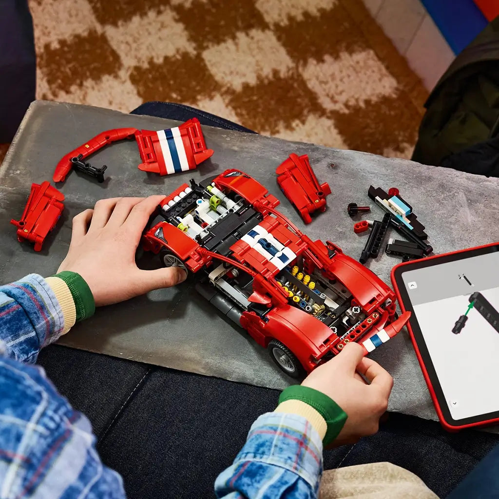 LEGO Technic Ferrari 488 Pista in red plastic with white and blue racing stripes is assembled by a young builder, with body panels removed and a tablet nearby.