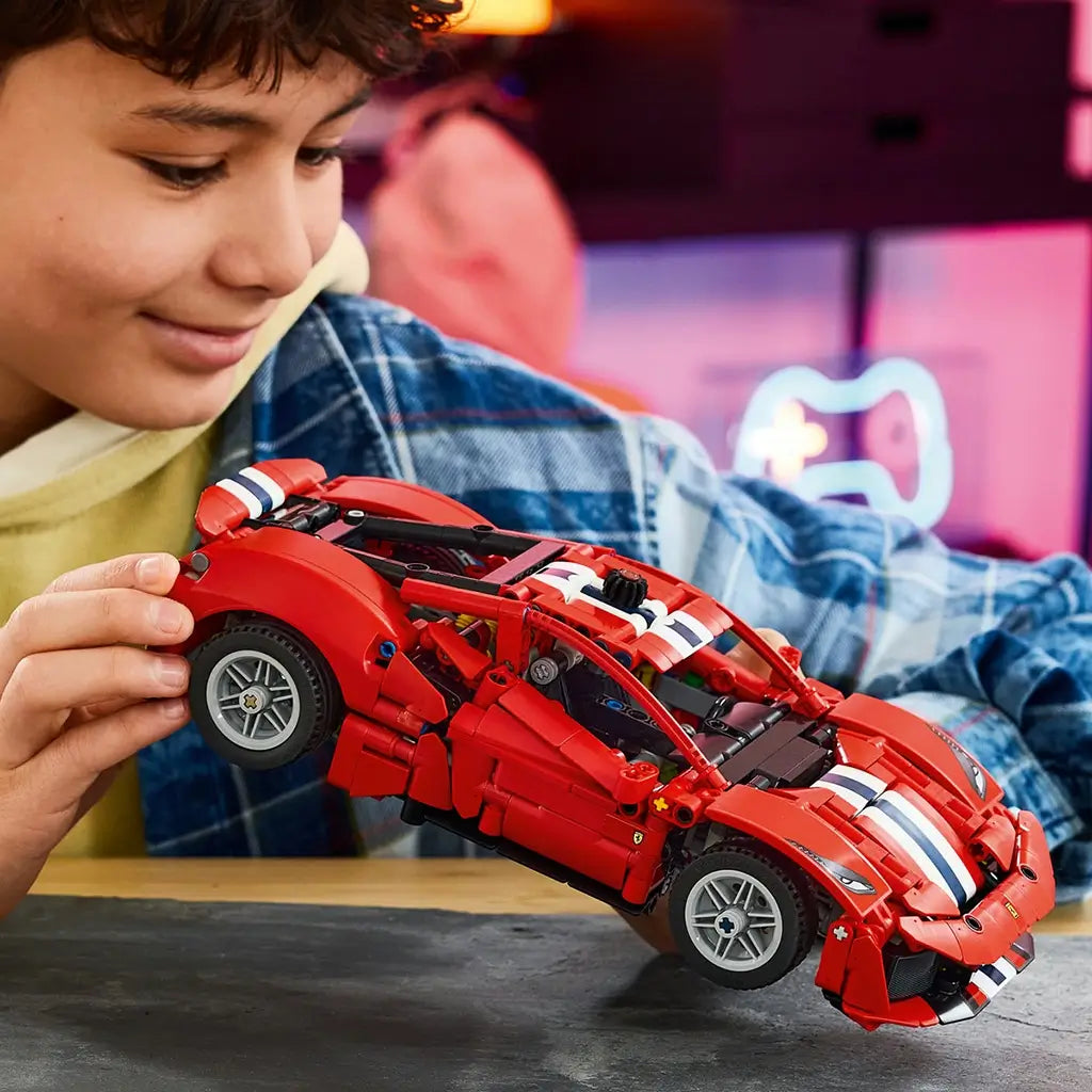 LEGO Technic Ferrari 488 Pista in red plastic with white and blue racing stripes is held by a young builder, showing its low body, silver wheels and detailed structure.