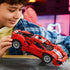 LEGO Technic Ferrari 488 Pista in red plastic with white and blue racing stripes is held by a young builder, showing its low body, silver wheels and detailed structure.