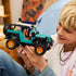 LEGO Technic Jeep Wrangler Rubicon toy shows a teal and black plastic SUV with textured tires and orange rims, held by a child while exploring features, representing hands on building play, set in a cozy indoor living room environment.