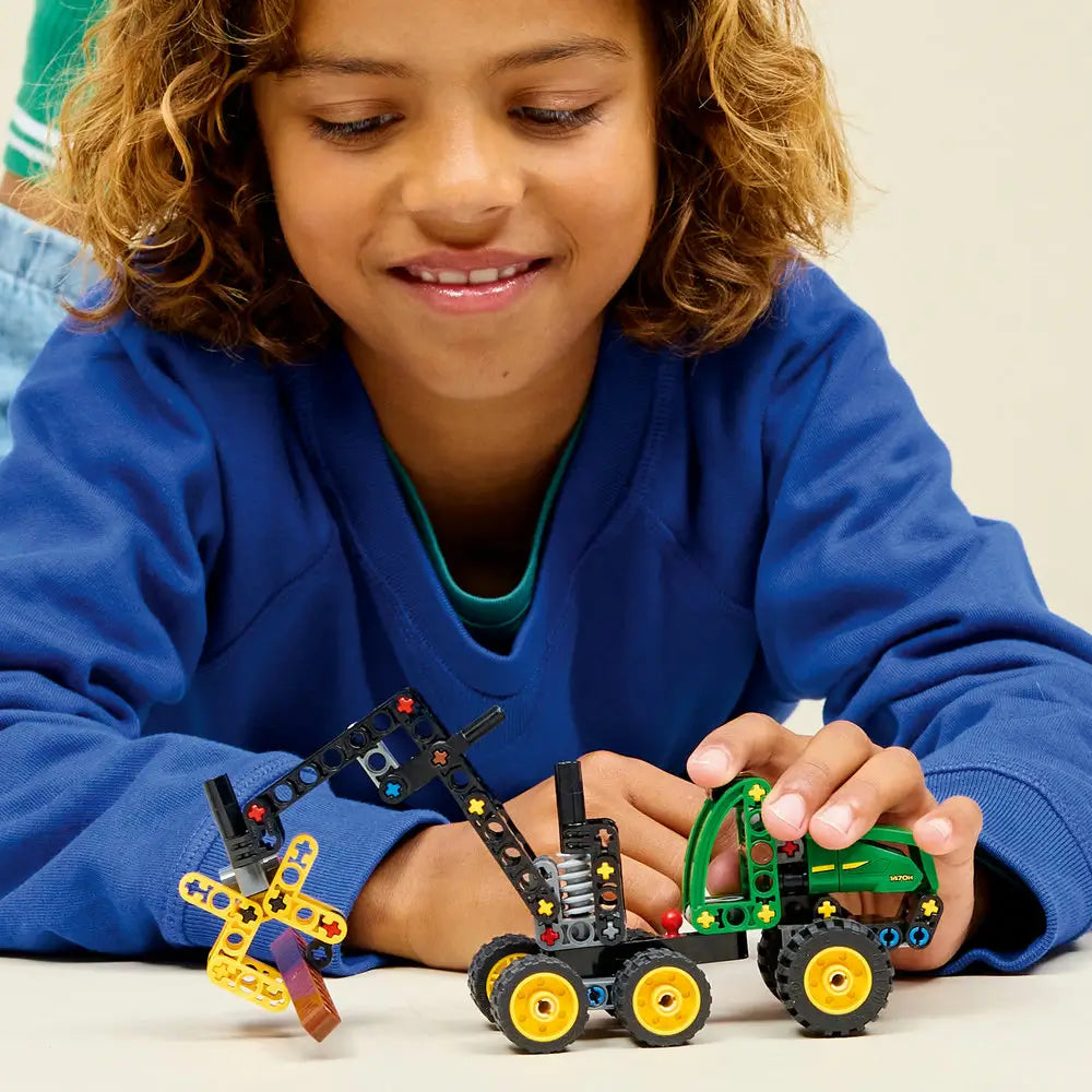 LEGO Technic John Deere 1470H Wheeled Harvester lifestyle image shows a smiling child playing with the completed forestry vehicle, highlighting the movable crane arm, rotating grabber, and realistic logging play features.