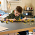 LEGO Technic Mighty Machines in yellow plastic are arranged across a gray table as a young builder plays with the small construction vehicles in a bright bedroom.