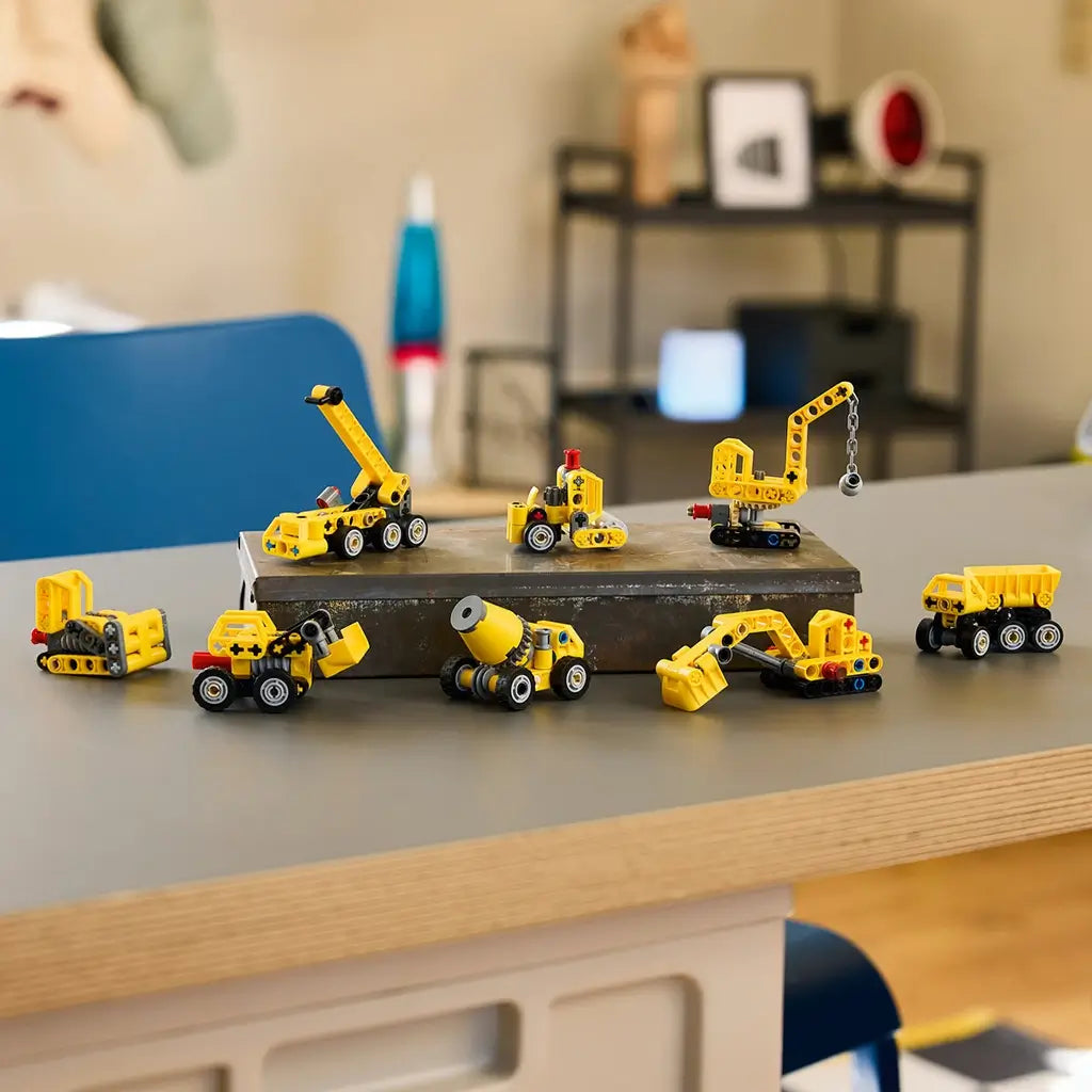 LEGO Technic Mighty Machines collection shows eight small yellow plastic construction vehicles, including cranes, loaders and trucks, displayed across a gray tabletop.