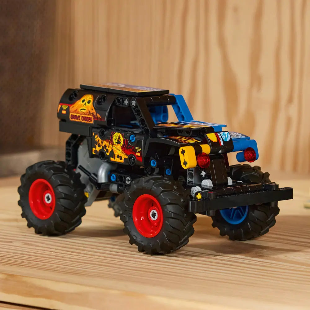 LEGO Technic Monster Jam Grave Digger truck displayed fully built with skull-and-flame body graphics, red wheel rims, black chassis, large treaded tires, and balanced monster truck proportions on a wooden surface.